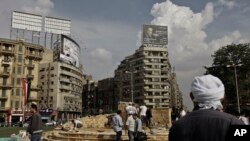 In this Sunday, Nov. 17, 2013 photo, an Egyptian man looks at municipality laborers working on a memorial base two days before the commemoration of deadly clashes with security forces in 2011, in Tahrir Square, Cairo. 