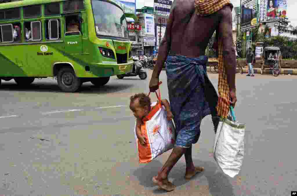Seorang laki-laki membawa anaknya di dalam sebuah tas saat ia menyeberang jalan di Bhubaneswar, India.