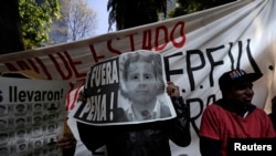 Demonstrator covers face with poster reading "Pena Out" during protest in support of 43 missing students outside office of Mexico's Attorney General, Mexico City, Nov. 27, 2014.