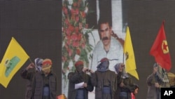 Des supporters masqués agitent des drapeaux du PKK devant un écran montrant le chef rebelle kurde emprisonné Abdullah Ocalan, Diyarbakir, Turquie, jeudi 21 mars, 2013.