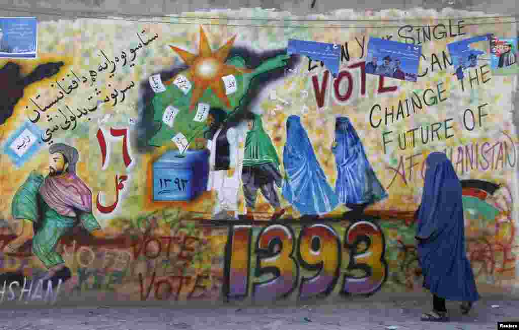 Seorang perempuan berjalan melewati grafiti yang mendorong masyarakat untuk memberikan suaranya di provinsi Kandahar, Afghanistan (30/3). (Reuters/ Ahmad Nadeem)