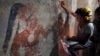 Conservator Angelyn Bass cleans and stabilizes the surface of a wall of a Maya house that dates to the 9th century A.D. The figure of a man who may have been the town scribe appears on the wall to her left. (Tyrone Turner © 2012 National Geographic)