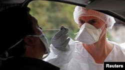 A medical worker administers a nasal swab to a patient at a drive-through testing site for coronavirus disease (COVID-19) near the hospital in Laval, France, July 15, 2020.