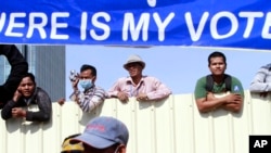 Cambodian workers look through a partition of a construction site below a banner which reads "Where is my vote" as supporters of opposition Cambodia National Rescue Party gather in Phnom Penh, file photo. 