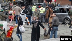 Women walk past as Lebanese army soldiers, gather at the site of Tuesday's explosion, in the Haret Hreik area in the southern suburbs of the Lebanese capital Beirut, Jan. 22, 2014.