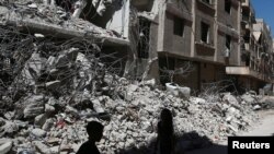 Des enfants marchent près des décombres d'immeubles détruits lors de bombardements dans la ville rebelle d'Aïn Tarma, dans la Ghouta orientale, en Syrie, le 19 juillet 2017.