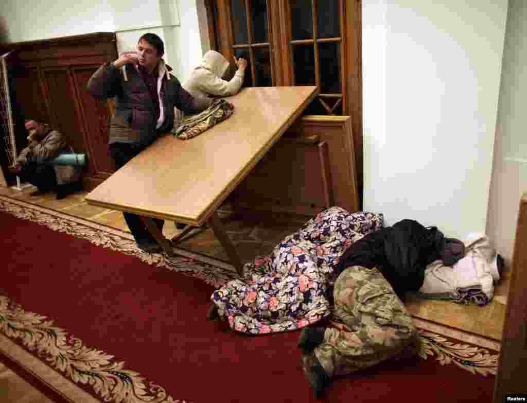 Protesters sleep on the floor as others look through a window for police inside Kyiv's city hall, Dec. 1, 2013.