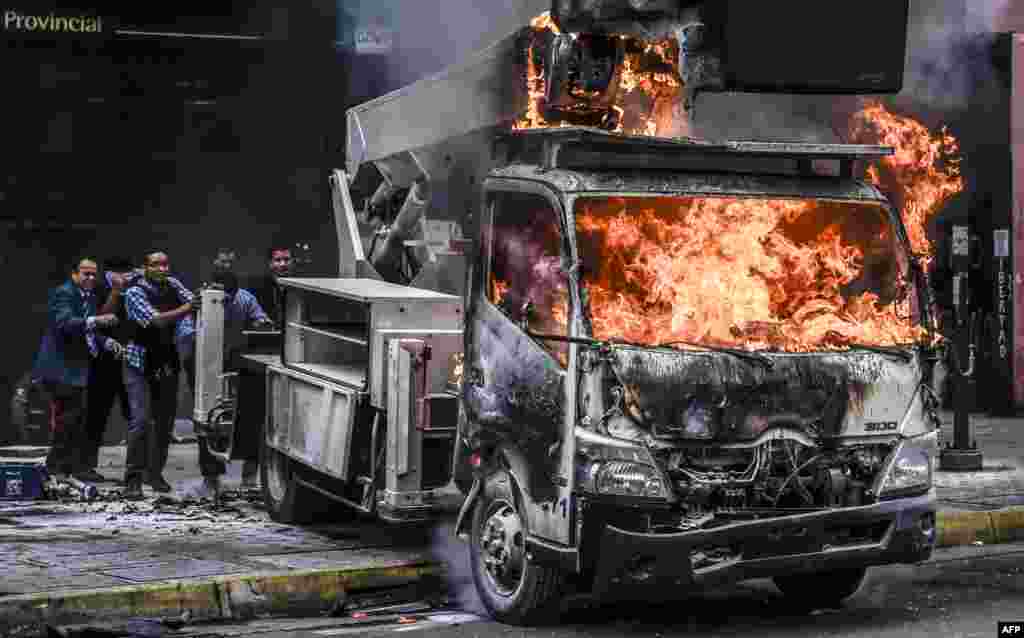 Para pekerja di komplek gedung pemerintah mendorong sebuah truk yang dibakar demonstran pada aksi protes menentang Presiden Nicolas Maduro di Caracas, Venezuela.