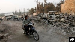 Burmese police officer rides a motorbike past debris of buildings and a truck destroyed during ethnic unrest between Buddhists and Muslims, as he provides security in Meikhtila, March 25, 2013.