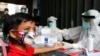 Seorang anak laki-laki mengenakan masker, menunggu disuntik menunggu petugas kesehatan melakukan tes antibodi virus corona di sebuah desa di Bali, Rabu, 27 Mei 2020. (AP Photo / Firdia Lisnawati)