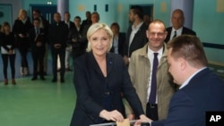 Pemimpin Fron Nasional yang berhaluan kanan dan capres Marine Le Pen sedang memasukkan surat suaranya ke kotak suara di Henin-Beaumont, utara France, didampingi oleh Front Nasional Henin-Beaumont, Steeve Briois, 23 April 2017. (Foto: dok).