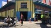 Customers sit outside the Caribbean Marketplace in Little Haiti, Miami, Florida. (Photo: S. Lemaire / VOA) 