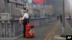 A traveler stands on a bridge near a display showing government propaganda in the fight against the COVID-19 viral illness in Beijing, China Thursday, Feb. 13, 2020. China is struggling to restart its economy after the annual Lunar New Year holiday…