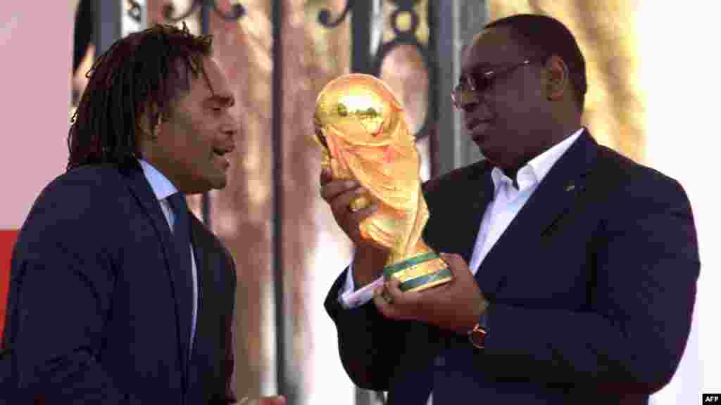 L'ancien footballeur international français Christian Karembeu présente le trophée de la Coupe du monde au président sénégalais Macky Sall lors d'une cérémonie à Dakar, le 11 mars 2018.