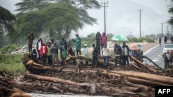 People stand on debris blocking a highway after River Muruny burst its bank following heavy rains in Parua village, about 85 km northeast of Kitale, in West Pokot county, western Kenya, Nov. 24, 2019.