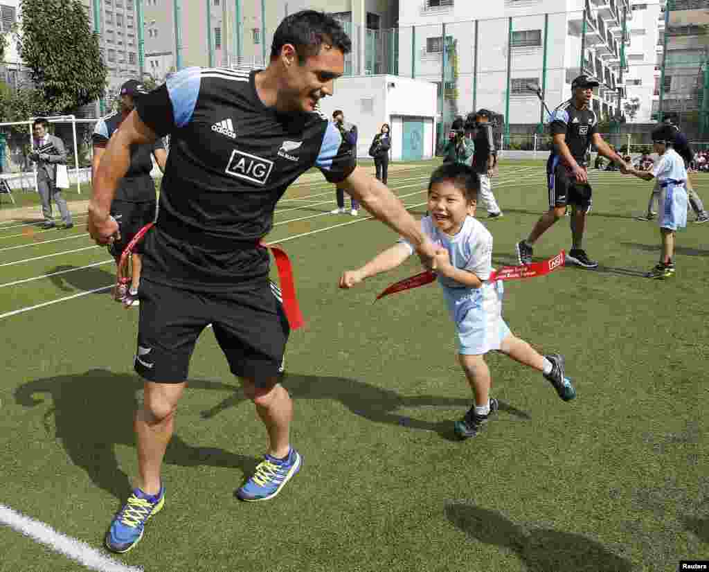 Pemain Tim All Blacks' dari Selandia Baru, Daniel Carter, tampak bermain bersama seorang murid dalam kunjungan Tim All Blacks ke SD Aoyama menjelang pertandingan persahabatan rugby internasional antara Selandia Baru dan Jepang hari sabtu di Tokyo.