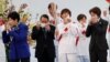 Tokyo Gov. Yuriko Koike, left, Tokyo 2020 Organizing Committee President Seiko Hashimoto, right, and attendees take off their face masks while preparing to pose for group photos during the Tokyo 2020 Olympic Torch Relay Grand Start.