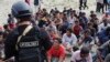 Seorang polisi berjaga-jaga saat pria etnis Rohingya duduk di pantai seusai mendarat di Aceh Besar, Minggu, 8 Januari 2023. Lebih dari 100 pengungsi Muslim Rohingya tiba di Aceh setelah perjalanan panjang dan berbahaya di atas perahu kayu. (AP/Muhammad Ahyar)