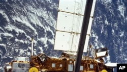 In this image provided by NASA this is the STS-48 onboard photo of the Upper Atmosphere Research Satellite (UARS) in the grasp of the RMS (Remote Manipulator System) during deployment, from the shuttle in September 1991. The satellite is 35 feet long, 15