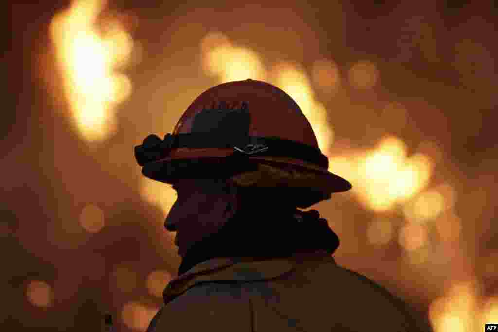 Seorang petugas pemadam kebakaran memantau kebakaran&quot;Colby Fire&quot; pada hari kedua di lereng bukit di atas Jalan Bebas Hambatan 39 di Azusa, California. Tiga orang telah ditangkap dengan tuntutan mengobarkan api tersebut yang sekarang telah membakar 1.700 hektar lahan dan beberapa rumah di San Gabriel Valley.