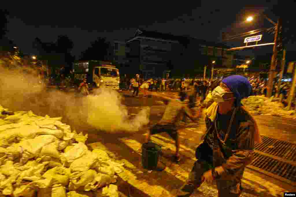 An anti-government protester throws a tear gas canister towards police from behind a barricade during clashes near the Government House in Bangkok, Dec. 1, 2013.