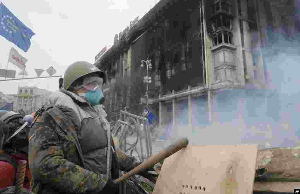 Seorang demonstran anti-pemerintah berdiri di belakang barikade dalam bentrokan dengan polisi di alun-alun Kyiv (19/2). (AP/Efrem Lukatsky)