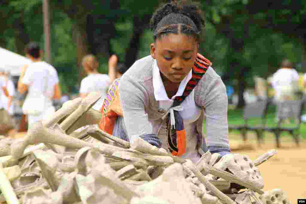 A girl selects artificial bones for display at the "One Million Bones" installation on the National Mall, Washington, D.C, June 8, 2013. (Jill Craig/VOA)