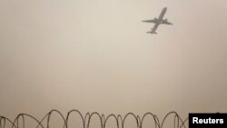 FILE - A plane flies in the polluted air above the airport fences in Beijing, Feb. 22, 2012. An IATAA official says a deal on limiting carbon dioxide emissions from aviation will likely be reached next year.