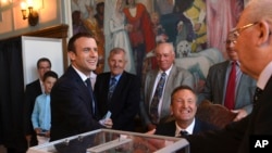 Presiden Perancis Emmanuel Macron, kiri, bersalaman dengan petugas pemilu setelah memberikan suaranya pada putaran kedua pemilu parlemen Perancis di Le Touquet, Perancis utara, Minggu, 18 Juni 2017. (Christophe Archambault/Pool Photo via AP)
