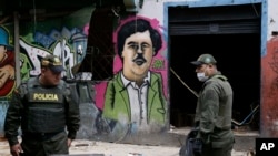 FILE - Police officers stand in front of a mural depicting the late drug kingpin Pablo Escobar, in the area known as El Bronx in downtown Bogota, Colombia, May 30, 2016. The area has been plagued by drug addicts and prostitution, including girls forced into sexual servitude.