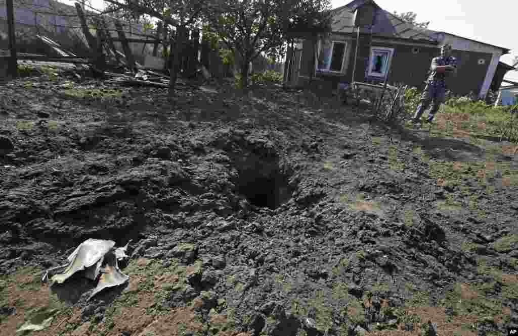 A local man stands next to a shell crater with his destroyed house in the background, in Donetsk, eastern Ukraine, Aug. 14, 2014.