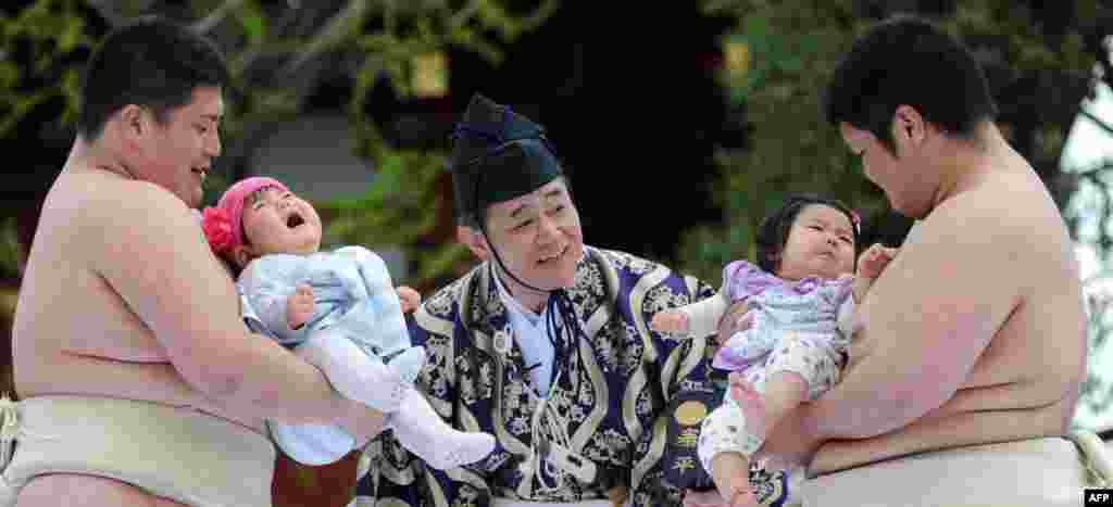 Dua mahasiswa pegulat sumo membawa bayi yang menangis di samping wasit (tengah) dalam acara Kompetisi 'Bayi Menangis' di kuil Sensoji di Tokyo, Jepang.