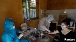 Medical specialists collect blood sample from a woman who has returned after travelling to Da Nang, at a rapid testing center for COVID-19 outside Hanoi, Vietnam, July 30, 2020.