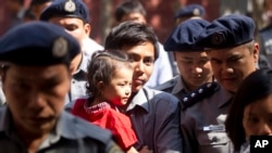 Jurnalis Reuters Kyaw Soe Oo (tengah) menggendong anak perempuannya, dikawal oleh polisi Myanmar pasca sidang pengadilan di Yangon, Myanmar (foto: dok).