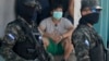 Una persona con máscara protectora observa mientras soldados y la policía acordonan el vecindario de Lincoln para evitar que los pobladores se vayan, después de que varias personas dieron positivo por el nuevo coronavirus, en Tegucigalpa.