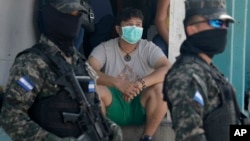 Una persona con máscara protectora observa mientras soldados y la policía acordonan el vecindario de Lincoln para evitar que los pobladores se vayan, después de que varias personas dieron positivo por el nuevo coronavirus, en Tegucigalpa.