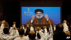 FILE - Hezbollah scouts raise their fists and cheer as they listen to a speech of Hezbollah leader Hassan Nasrallah, via video link, during a rally in southern Beirut, Lebanon, April 22, 2019. 