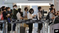 Para penumpang mengenakan masker, antri sebelum memasuki pesawatnya di bandara Gimpo, Seoul, Korea Selatan, 27 Mei 2020. (Foto: dok).