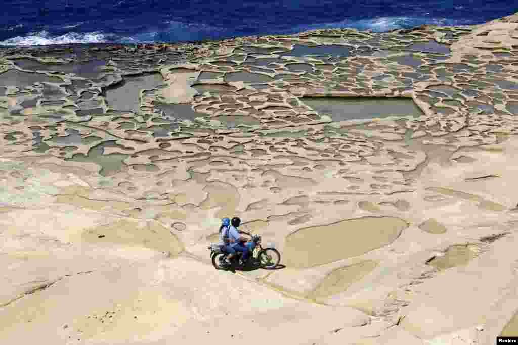 Dua orang naik sepeda motor di dekat kawasan 'Panci Garam', yang diyakini telah digunakan untuk membuat garam laut sejak zaman Romawi, di luar desa Marsalforn, di pantai utara pulau Gozo, Malta.