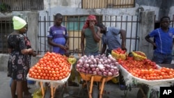 une femme achète des tomates et des oignons à des marchands ambulants à Lagos, au Nigéria, le 13 avril 2020. Le confinement dû à la lutte contre le covid-19 limite la circulation des personnes, rendant difficile l'approvisionnement. (Photo AP / Sunday Alamba)