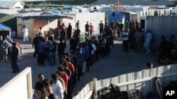 FILE- Migrants line up to receive their daily food distribution in a makeshift camp in Calais, northern France. 