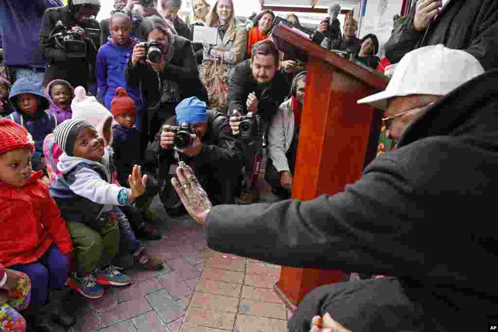 Archbishop Desmond Tutu, right, holds out his hand as he interacts with children during celebrations of former South African President Nelson Mandela's birthday in Cape Town, South Africa, July 18, 2014.