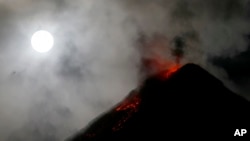The super blue blood moon sets before dawn as lava cascades down the slopes of Mount Mayon volcano during a mild eruption as seen from Sto. Domingo township, Albay province around 340 kilometers (200 miles) southeast of Manila, Philippines, Feb. 1, 2018.