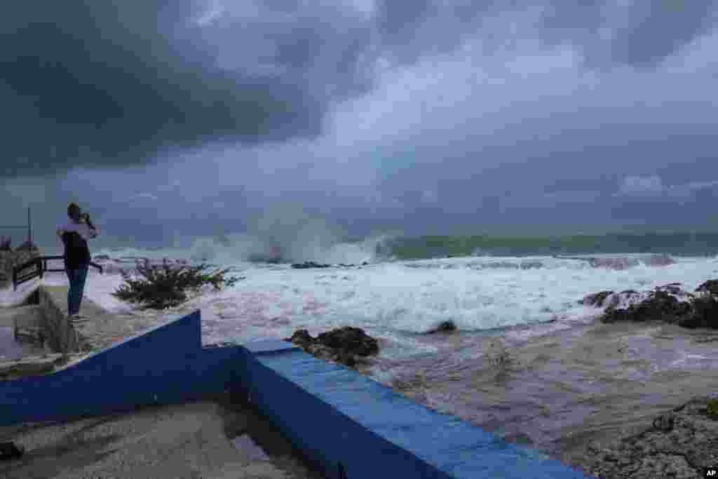 A woman takes photos of waves crashing against a seawall as Hurricane Ian passes through George Town, Grand Cayman Island, Sept. 26, 2022.