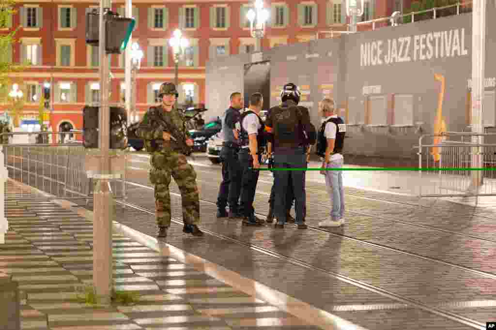 Police officers and a soldier stand by the sealed off area of an attack after a truck drove on to the sidewalk and plowed through a crowd of revelers who'd gathered to watch the fireworks in the French resort city of Nice, southern France, Friday, July 15