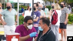 FILE - Carlos Anacleto closes his eyes as he receives the Pfizer COVID-19 vaccine from nurse Jorge Tase, as others wait their turn, Aug. 4, 2021, in Miami Beach, Fla. 