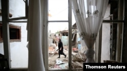 A woman walks past a house damaged by recent shelling during a military conflict over the breakaway region of Nagorno-Karabakh, in the city of Ganja, Azerbaijan, Oct. 6, 2020.