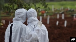 Des membres de la famille regardent des ouvriers enterrer un cercueil dans la section spéciale du cimetière de Padurenan qui a été ouverte pour faire face à l'augmentation des décès dû à l'épidémie de coronavirus à Bekasi, en Indonésie, jeudi 17 juin 2021.