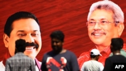 Supporters of Sri Lanka Podujana Peramuna (SLPP) party presidential candidate Gotabaya Rajapaksa walk past cut-out placards of the Rajapaksa brothers, Gotabaya (R) and Mahinda (L), in Colombo on November 17, 2019.