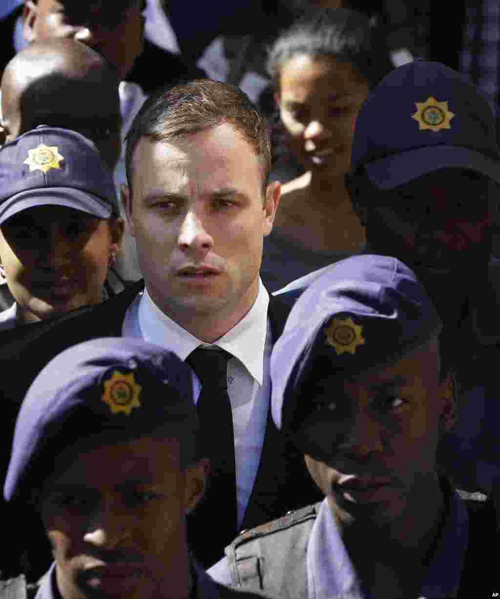 Oscar Pistorius is escorted by police officers as he leaves the high court in Pretoria, South Africa, Oct. 16, 2014.